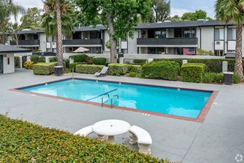 A swimming pool surrounded by a white table and chairs.